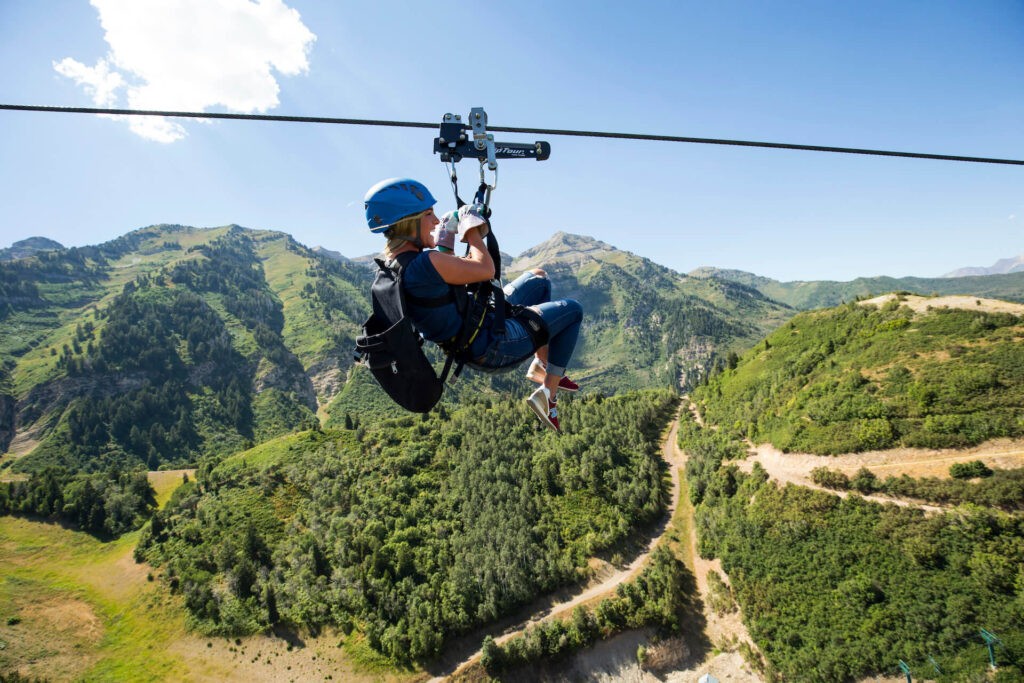 Person ziplining during the summer at Sundance Mountain Resort with mountains in the background