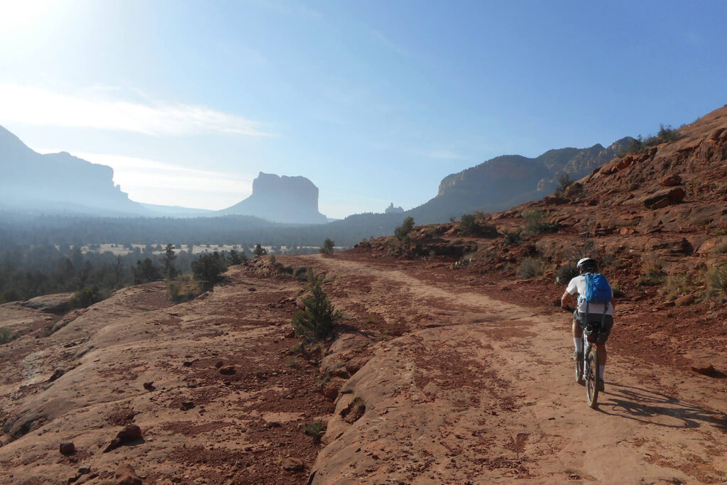 Person biking down trail surrounded by rock formations near Sedona, Arizona